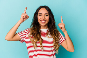 Young mexican woman isolated on blue background indicates with both fore fingers up showing a blank...
