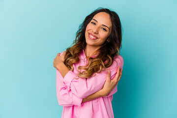 Obraz premium Young mexican woman isolated on blue background hugs, smiling carefree and happy.