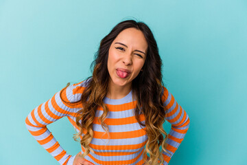 Young mexican woman isolated on blue background funny and friendly sticking out tongue. - obrazy, fototapety, plakaty