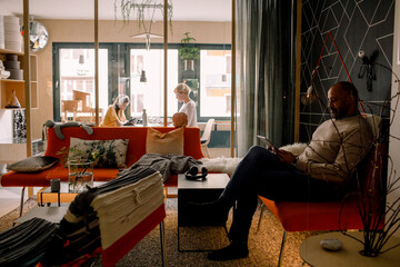 Mature man using digital tablet with woman and daughter in background