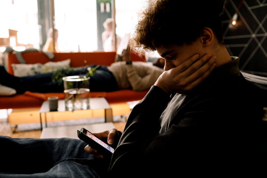 Teenage boy using smart phone while father lying on sofa in living room