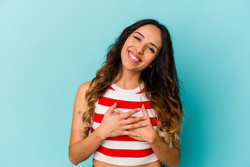 Young mexican woman isolated on blue background has friendly expression, pressing palm to chest....