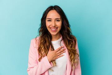 Young mexican woman isolated on blue background laughs out loudly keeping hand on chest.