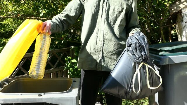 One person performing a selective sorting of household waste in recycling bins. Man putting plastic bottles in a yellow container and garbage in a bag in a green container.