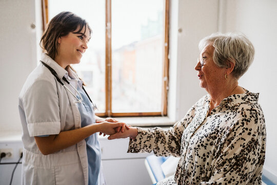 Smiling female healthcare worker looking at senior patient talking while holding hands