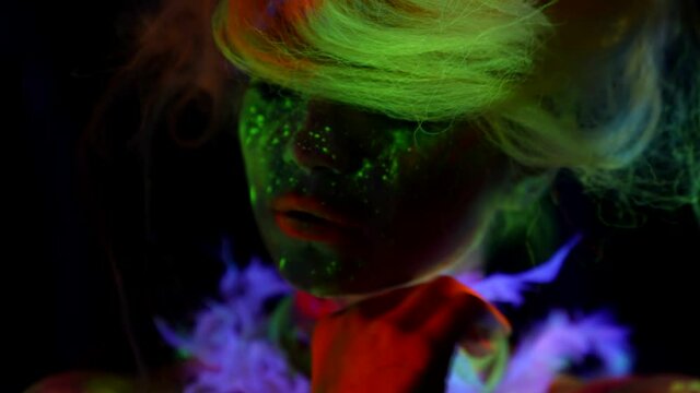 bright neon paints on face of young woman in UV light, image for Halloween