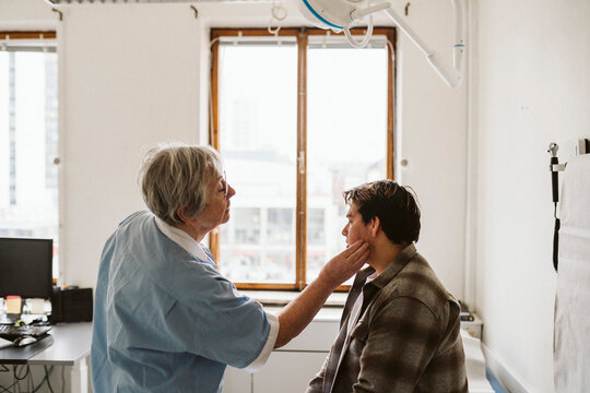 Senior female healthcare worker examining male patient's neck at medical clinic