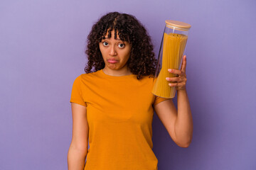 Young mixed race woman holding spaghetti isolated on purple background shrugs shoulders and open eyes confused. - obrazy, fototapety, plakaty
