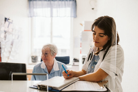 Female healthcare worker writing prescription while standing by senior nurse