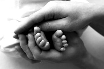 Feet of a newborn in the hands of a father, parent. Studio photography, black and white. Happy family concept.