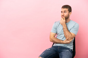 Young man sitting on a chair over isolated pink background thinking an idea while looking up