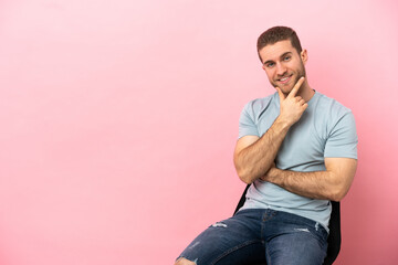 Young man sitting on a chair over isolated pink background happy and smiling