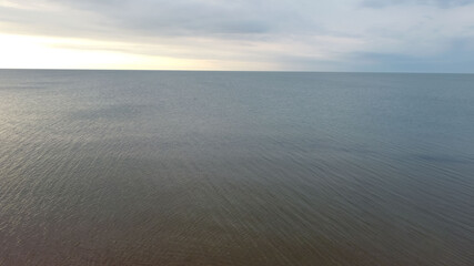 Aerial view of the sky and the water smoothness of the southern sea to the horizon with orange sunset reflexes for a natural background