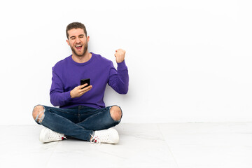 Young man sitting on the floor with phone in victory position