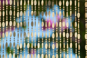 A beautiful beaded curtain hanging in a doorway with an out of focus background of a bougainvillea bush
