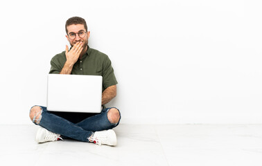 Young man sitting on the floor happy and smiling covering mouth with hand