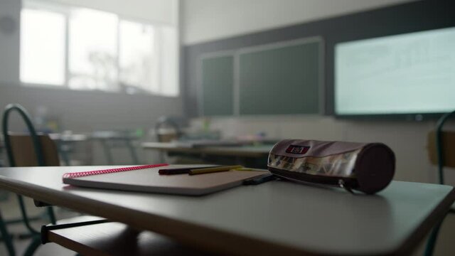 Notebook, pens and pencil case on desk in classroom. School supplies on table