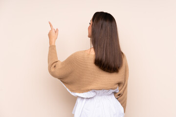 Young caucasian woman isolated on beige background pointing back with the index finger