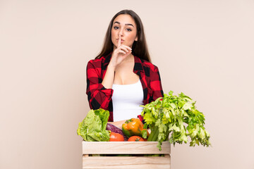 Farmer with freshly picked vegetables in a box isolated on beige background doing silence gesture