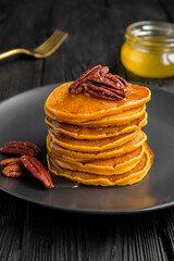 Homemade pumpkin pancakes with pecans in the black plate on the dark  background