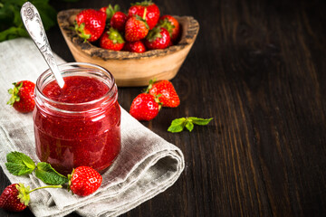 Strawberry jam in the glass jar with fresh berries at wooden table.