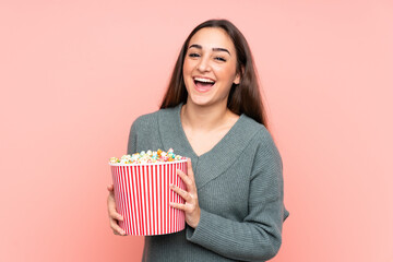 Young caucasian woman isolated on pink background holding a big bucket of popcorns