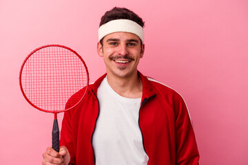 Young caucasian man playing badminton isolated on pink background happy, smiling and cheerful.