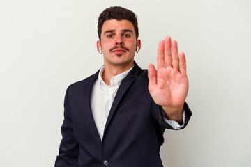 Young business caucasian man wearing wireless headphones isolated on white background standing with outstretched hand showing stop sign, preventing you.