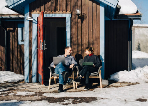 Businessman and businesswoman discussing while sitting in front of vacation home during winter