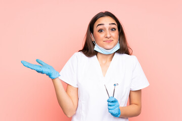 Woman dentist holding tools isolated on pink background having doubts with confuse face expression