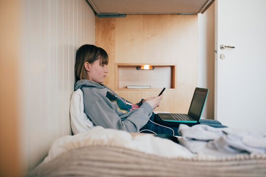 Teenage girl sitting with laptop using smart phone in vacation home