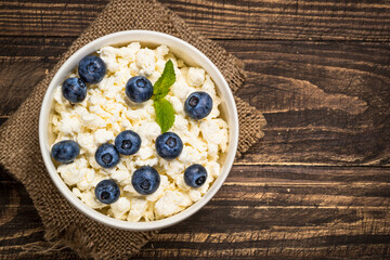 Curd or cottage cheese with blueberry in bowl at wooden table. Top view with copy space. Healthy breakfast.