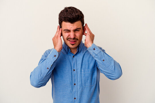 Young caucasian man isolated on white background covering ears with fingers, stressed and desperate by a loudly ambient.