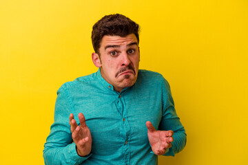 Young caucasian man isolated on yellow background shrugs shoulders and open eyes confused.