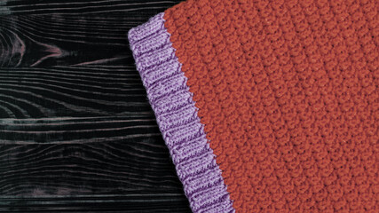Fabric knitted from red and purple threads on a dark wooden background top view of kopi space. The texture of the knitted fabric