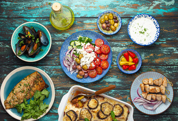 Assorted Greek dishes on rustic wooden background from above, moussaka, grilled fish, souvlaki, greek salad, steamed mussels with herbs, appetizers of Greece from above 