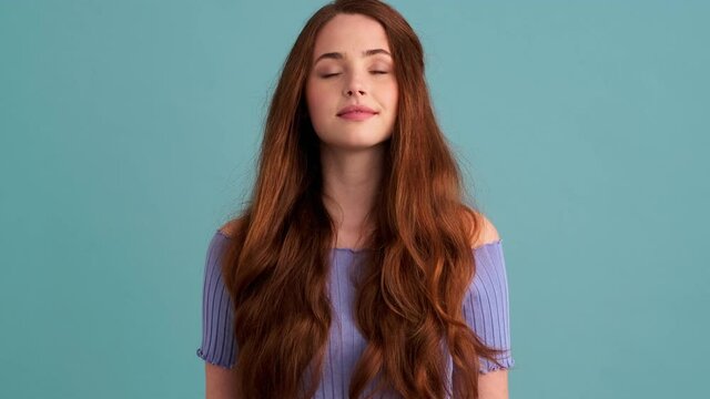 A calm woman is holding hands in dzen gesture standing isolated over blue wall in the studio