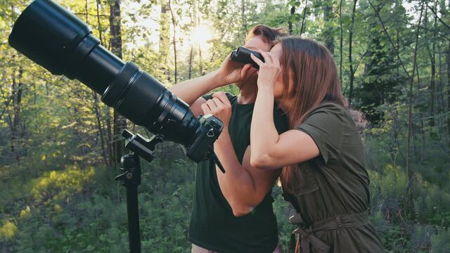 Birdwatching in park. Couple watch birds with binoculars and camera with telephoto lens. Amateur birdwatchers spot birds in the spring park