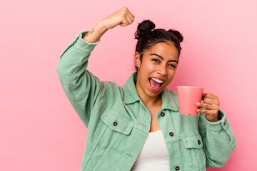 Young latin woman holding a mug isolated on pink background raising fist after a victory, winner concept.