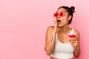Young latin woman holding an ice cream isolated on pink background is saying a secret hot braking news and looking aside