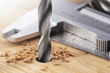 Drill bit making hole in wooden oaks plate, with ruler and caliper, pencil .