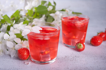 Strawberry cold refreshment lemonade with ice cube. White apple blossoms on the background. Spring concept.
