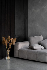 Dry plants in vase standing near grey couch