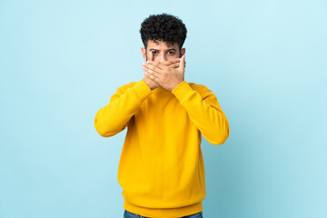 Young Moroccan man isolated on blue background covering mouth with hands