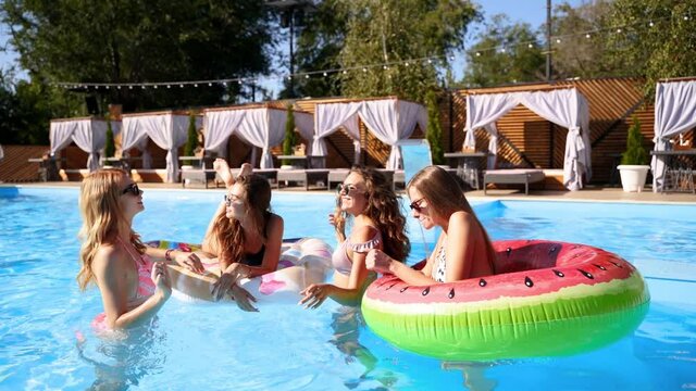 Beautiful hot pretty girls in bikini have pool party dancing with inflatable watermelon floaty mattress. Glamour fitted women in swimwear, sunglasses have fun relaxing on sunny summer day. Slow motion