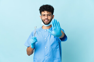 Moroccan dentist man holding tools isolated on blue background making stop gesture