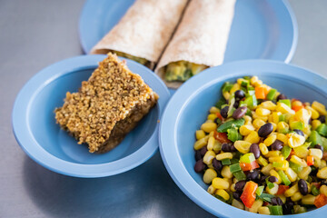 Selective focus. Two plastic dishes filled with a piece of cake and some colorful vegetables. Lunch time in a kindergarten. Focus on foreground.