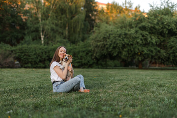 Fototapeta premium Portrait of a happy and crazy Jack Russell Terrier dog. Smooth coat of red color. a girl with brown hair in jeans and a T-shirt is playing with a dog. Cute and beautiful dog has fun outdoors.