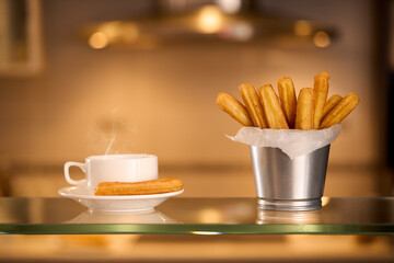 Homemade sweet churros pastries with sugar and cinnamon, a cup of chocolate on a kitchen background in blur