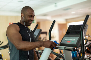 Black male athlete cleaning a cardio machine with disinfectant at the gym. Selective focus.